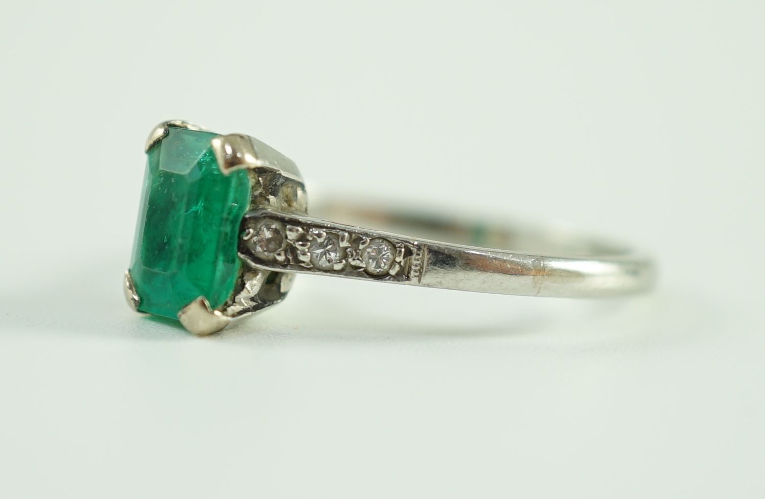 A white gold and single stone emerald ring, with six stone diamond set shoulders